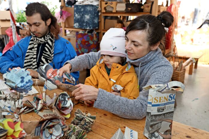 Dia Carrasco Soto und Christin Ferch mit Tochter Elsa basteln aus SachsenSonntagzeitungen Lampen, Taschen und Bl&uuml;ten. Foto: Andr&eacute; Kempner