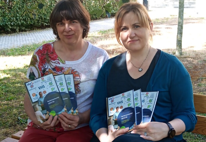 web-VHSABG_NeuesProgrammheft_HS2025_03 Die VHS-Mitarbeiterinnen Ute Rüdiger (l.) und Ludmilla Galaiko präsentieren das Programmheft für das Herbstsemester. Foto: Michael Hein
