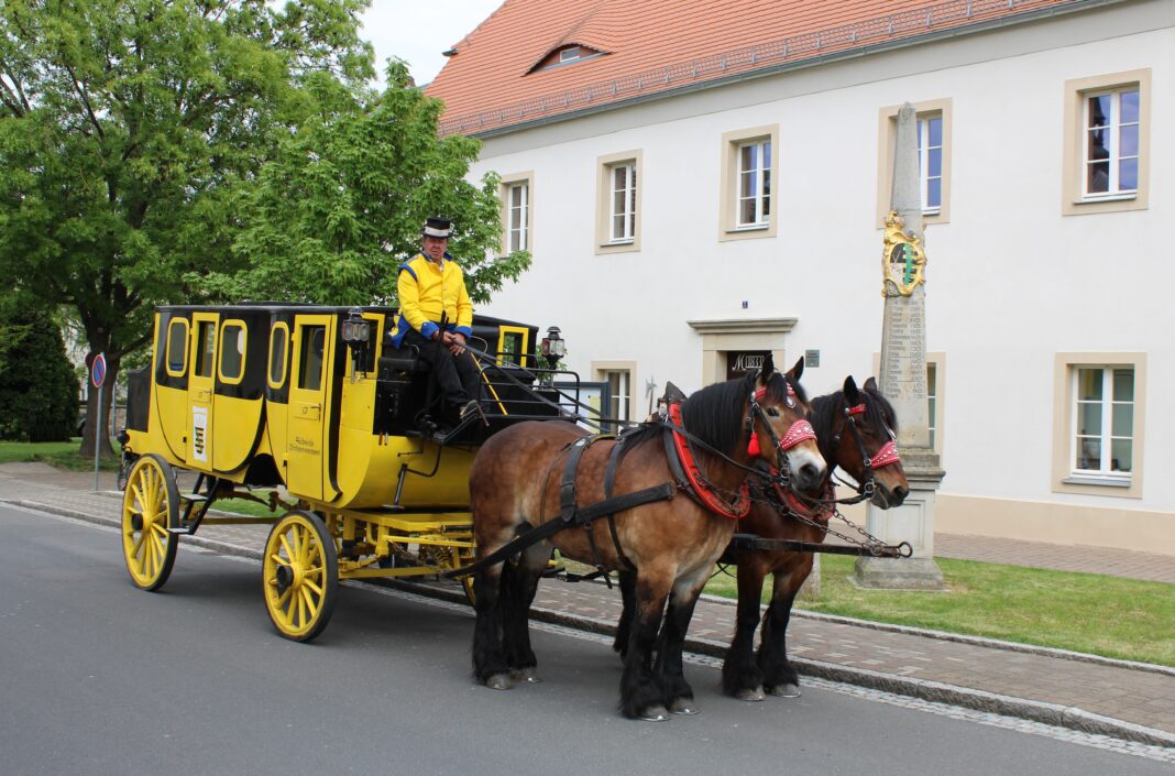Die Postkutsche neben der M&uuml;gelner Postmeilens&auml;ule im Mai 2025. Zum Jubil&auml;umsfest am 3. Mai sollen vier der &bdquo;Gelben Wagen&ldquo; in M&uuml;geln zusammentreffen. Foto: Jan Seelig