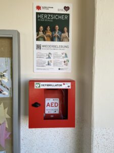 Der neue Defibrillator der Arthur-Becker-Oberschule h&auml;ngt gut sichtbar im ersten Obergeschoss &ndash; erg&auml;nzt durch eine Tafel des Projekts &bdquo;Herzsicher in der Schule&ldquo;, die die Wiederbelebung in vier Schritten erkl&auml;rt. Foto: Nannette Hoffmann 