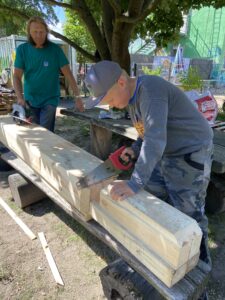 Elias s&auml;gt an der gro&szlig;en Holz-Heuschrecke f&uuml;r den Gemeinschaftsgarten &ndash; unterst&uuml;tzt von einem Betreuer, der mit der Elektros&auml;ge die groben Zuschnitte &uuml;bernimmt. Foto: Nannette Hoffmann