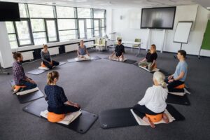 Die Teilnehmerinnen und Teilnehmer der Achtsamkeitskurse medi-tieren gemeinsam auf Yogamatten. Foto: Christian Hüller